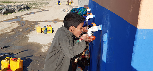 Children cupping their hands around taps in a wall