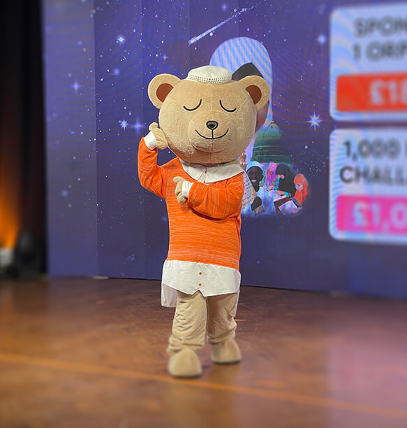 A cute bear mascot in an orange outfit performing a dance or greeting, with a digital backdrop in the background displaying challenges and goals.