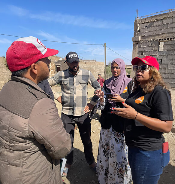 A group of people, including aid workers, talking to local residents in a crisis area.