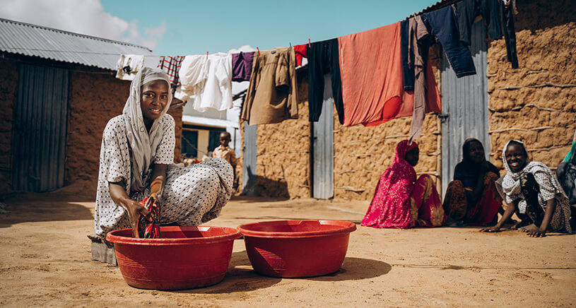 A woman smiles at the camera while washing clothes.