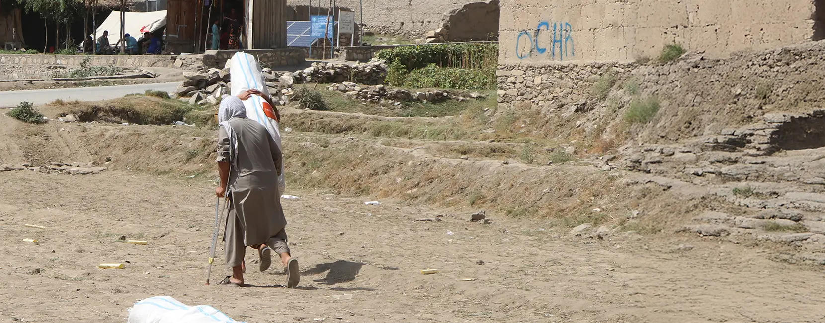 A man with crutches carries emergency aid supplies in a rural area of Afghanistan, supported by Penny Appeal