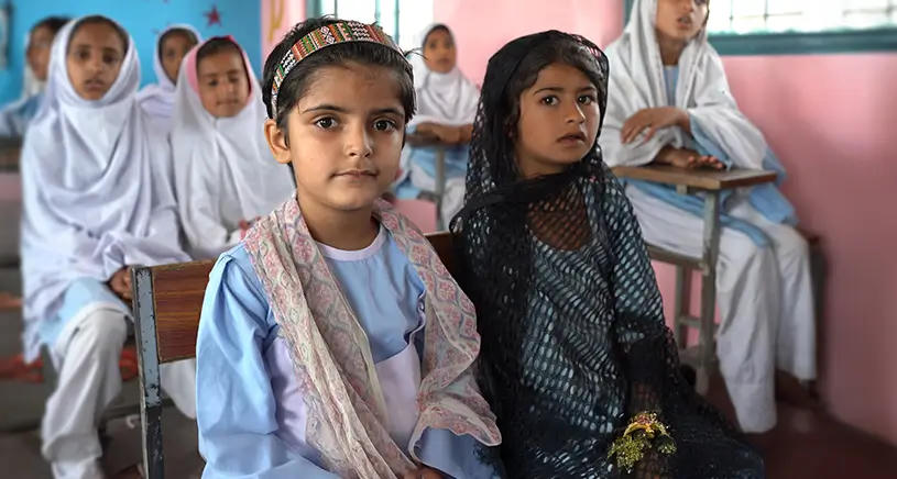 Two young girls in traditional clothing sit in a classroom
