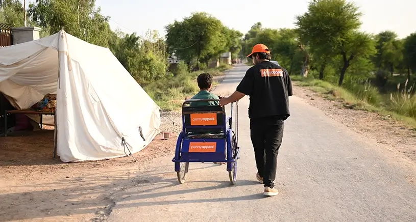A Penny Appeal worker pushes a man in a wheelchair.