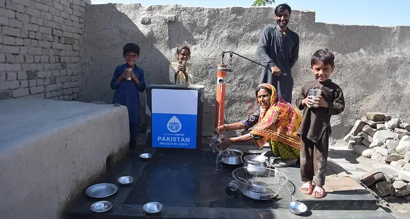 A smiling family collecting water from a well sponsored by Penny Appeal donors.