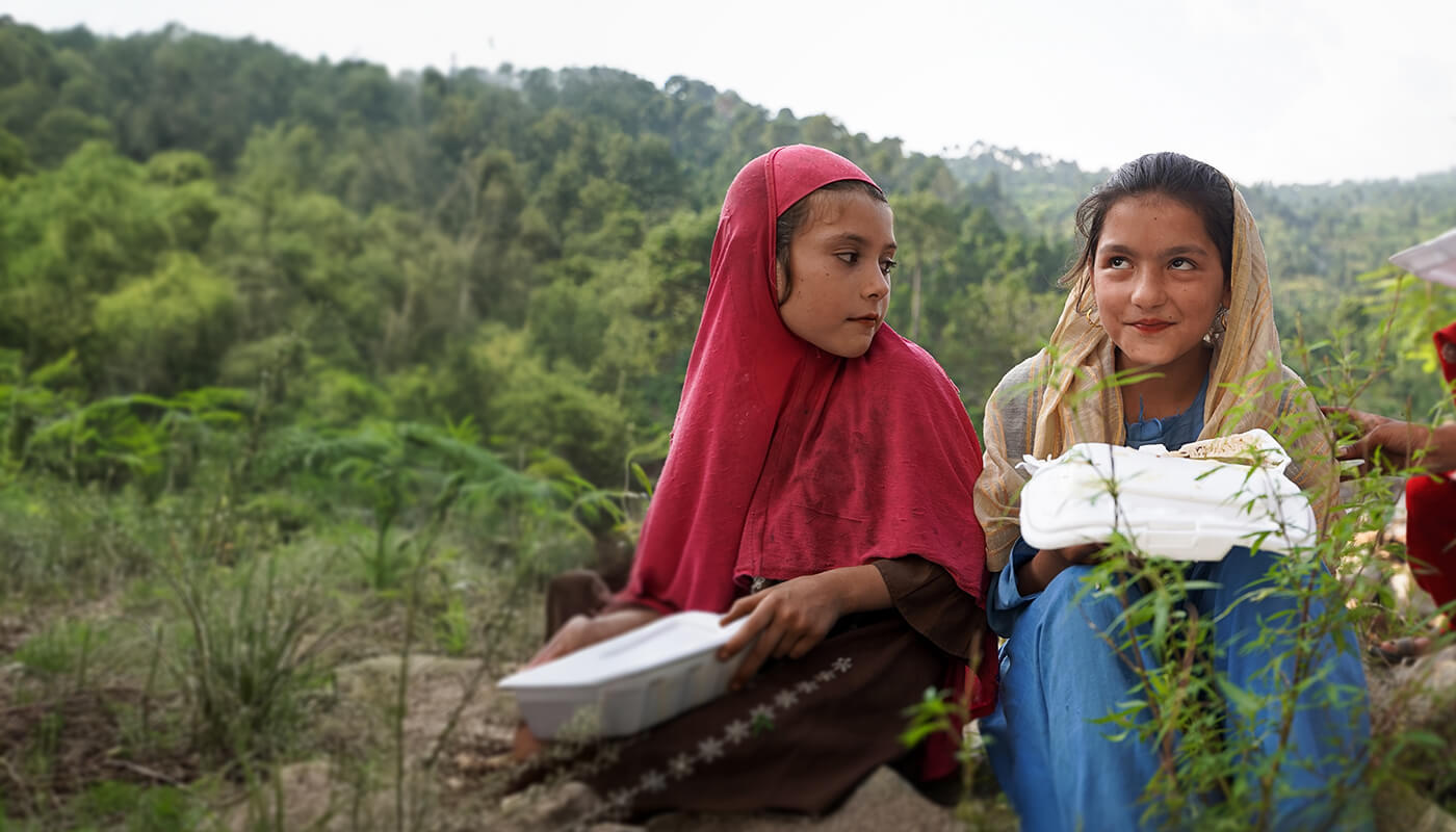 Two girls share a meal outdoors as part of Penny Appeal's Feed Our World program
