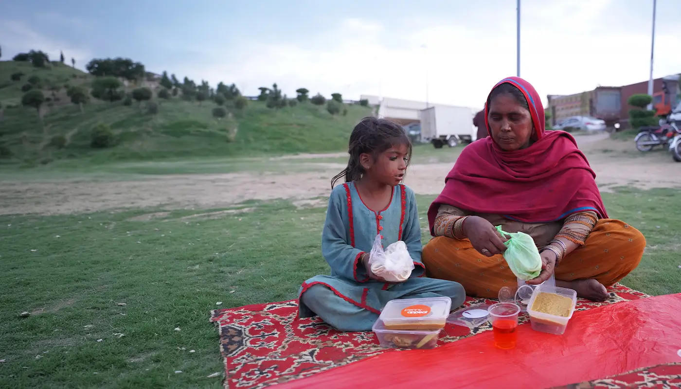 A mother and daughter eat food together while sat outside.