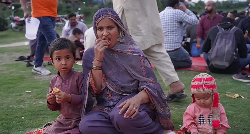 A women and children sit on the grass eating.