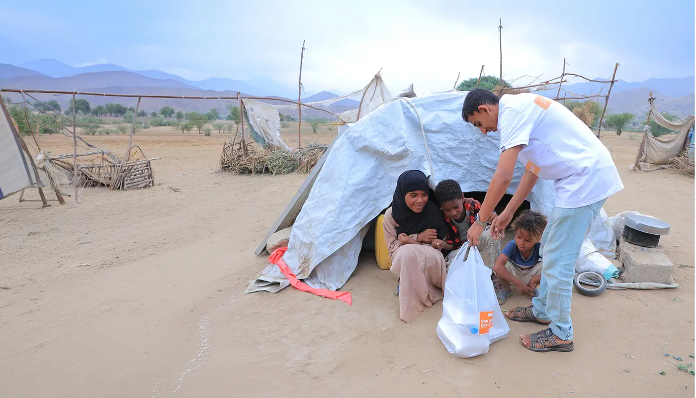 A family in a makeshift tent receive a donation of food from Penny Appeal.