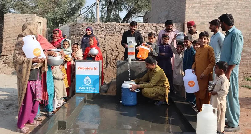 A group of people gather around a well installed by Penny Appeal.