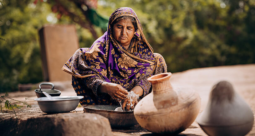 A woman sits on the ground washing her hands.