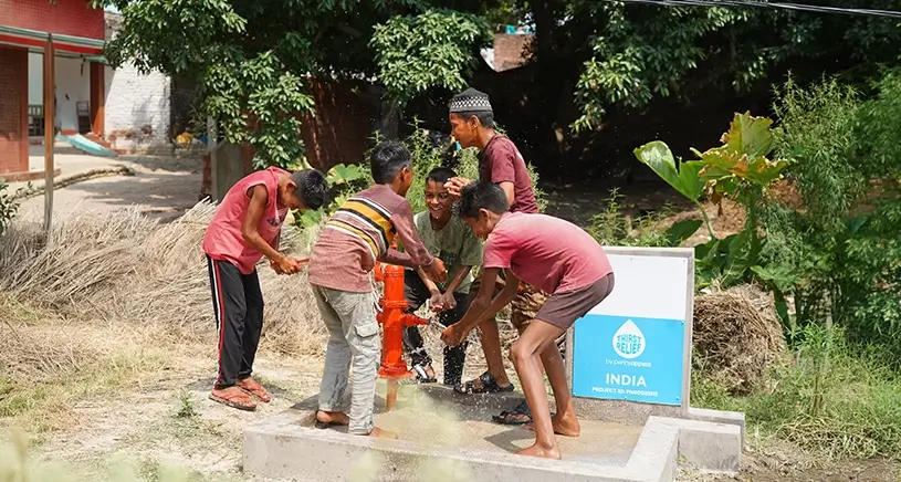A group of children play in the water coming from a well built by Penny Appeal.