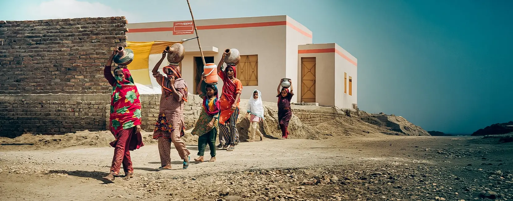 A group of women walk in a line with water jugs on their heads.