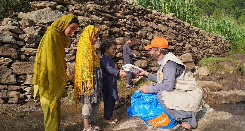 A Penny Appeal aid worker crouches down to hand food to a small group of children.