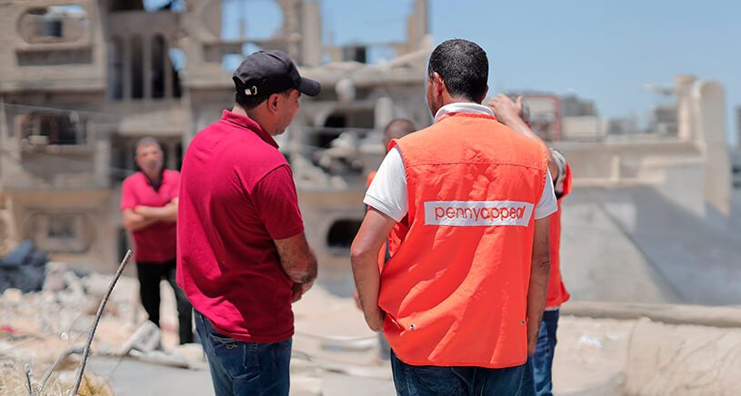 This image shows humanitarian aid workers from Penny Appeal, a charity organization, on the ground in what appears to be a conflict- or disaster-affected area.