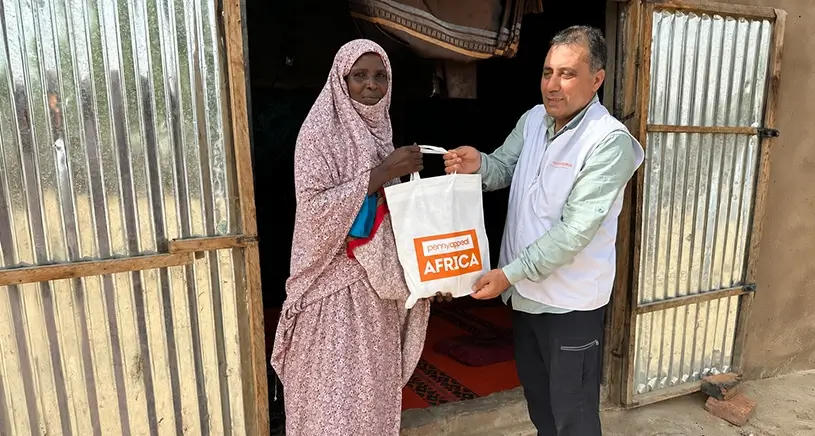 A man hands a woman a bag of Qurbani meat with Penny Appeal Africa written on the front.