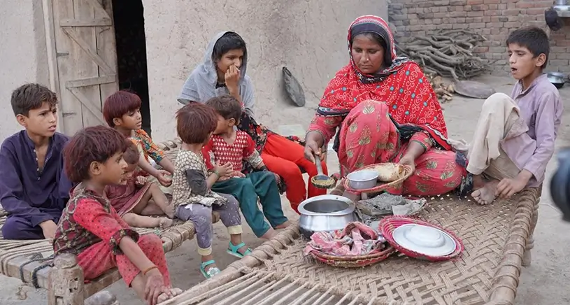 A group of children gather round as a woman cooks a meal.