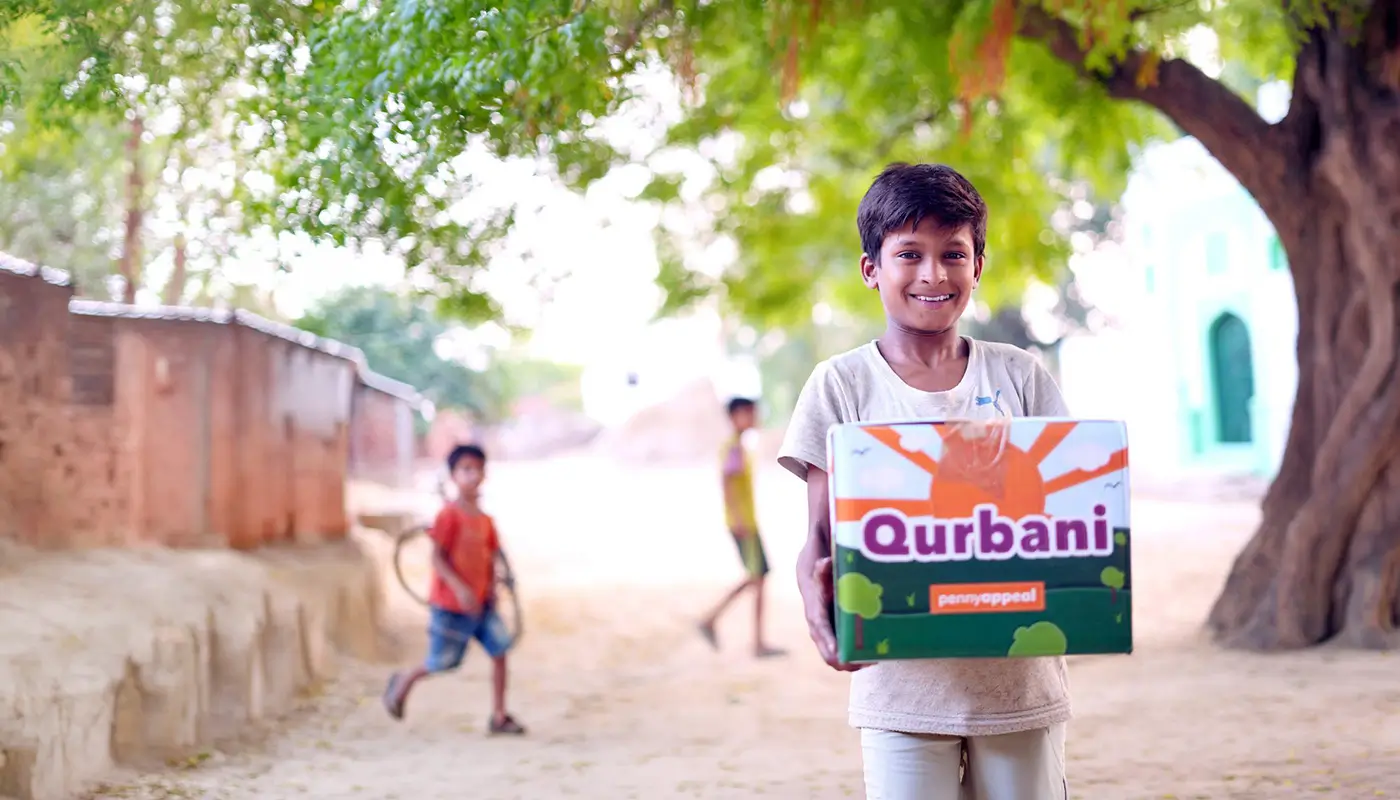 A smiling child hold a Qurbani box from Penny Appeal.