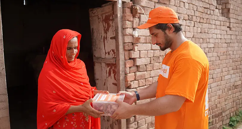 A Penny Appeal aid worker hands a woman Qurbani meat from Penny Appeal.