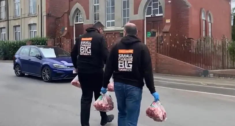 Two Penny Appeal workers walk away from the camera carrying bags of Qurbani meat.