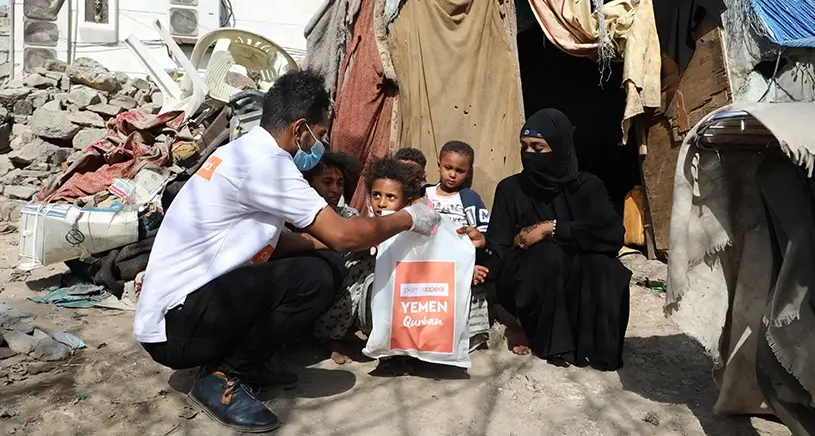 A Penny Appeal aid worker hands a bag of Qurbani meat to a family outside of a makeshift tent.