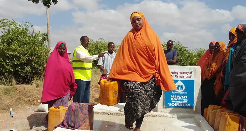 A woman in orange clothing carries jugs of water.