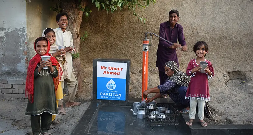 A smiling family gather around a well built by Penny Appeal.