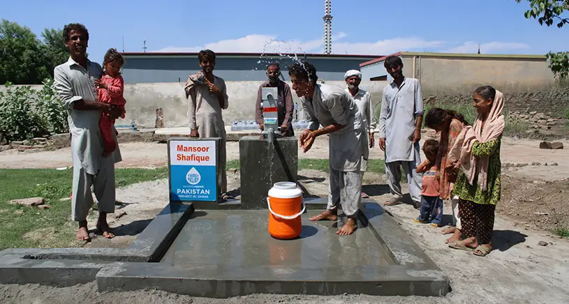 A group of people gathered around a deep well built by Penny Appeal.