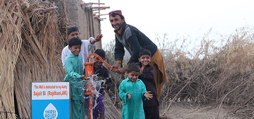 Man pumping a well with children playing in the water
