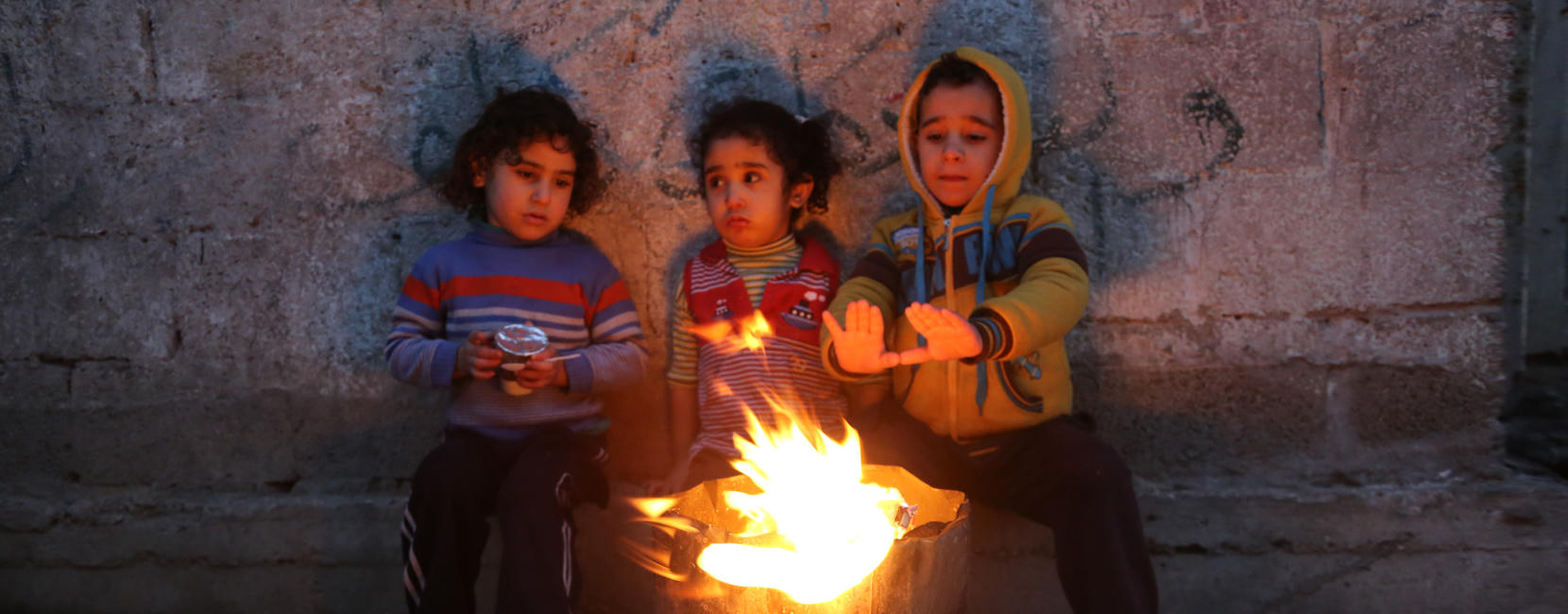 A group of small children gather around a fire, warming their hands.