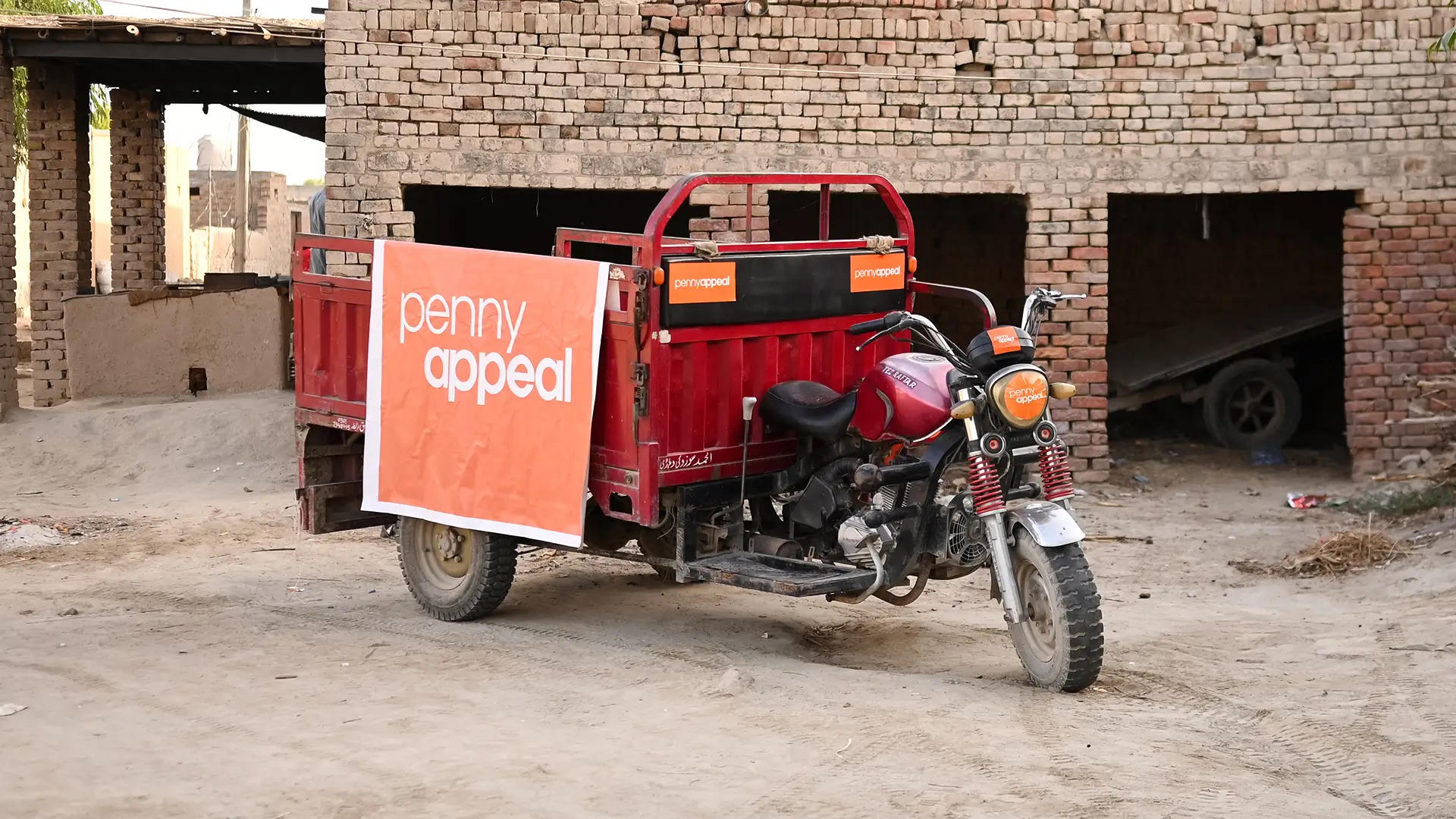 A red rickshaw with a large orange Penny Appeal logo on the side.