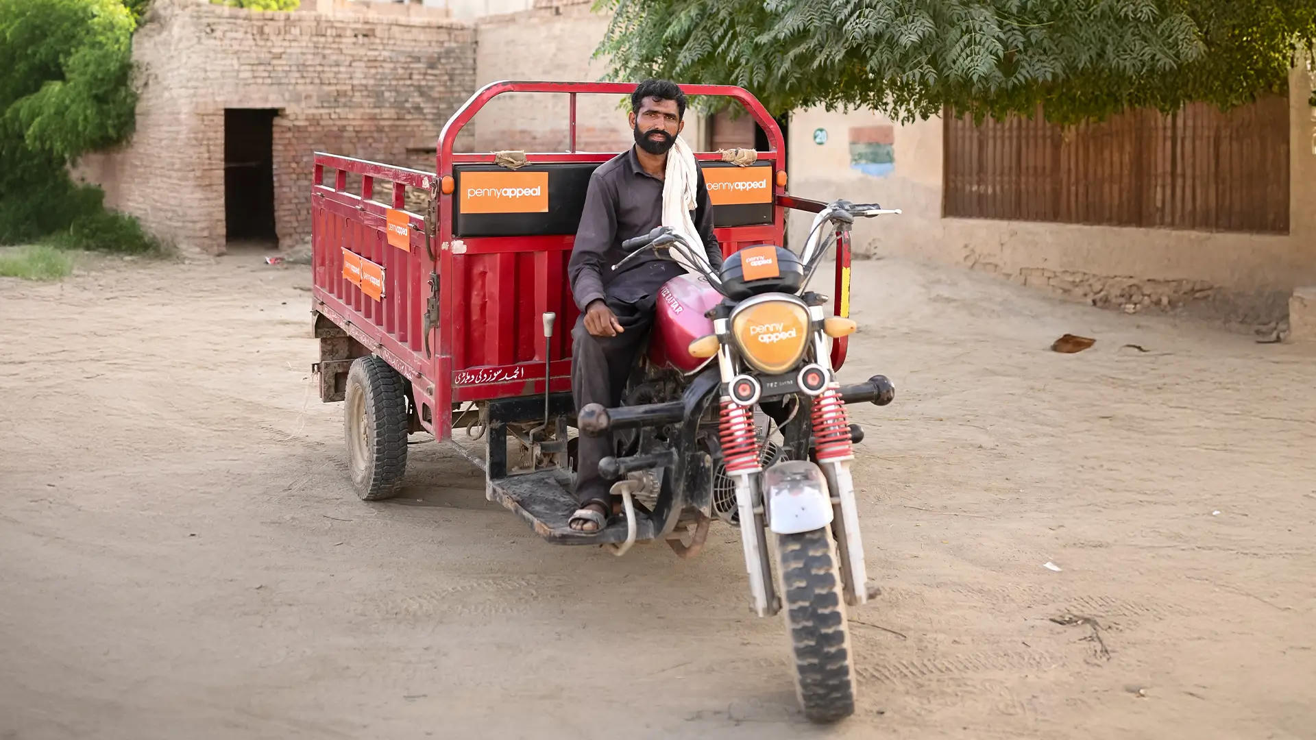 A man sits on a red rickshaw with an orange Penny Appeal logo on the front and sides.