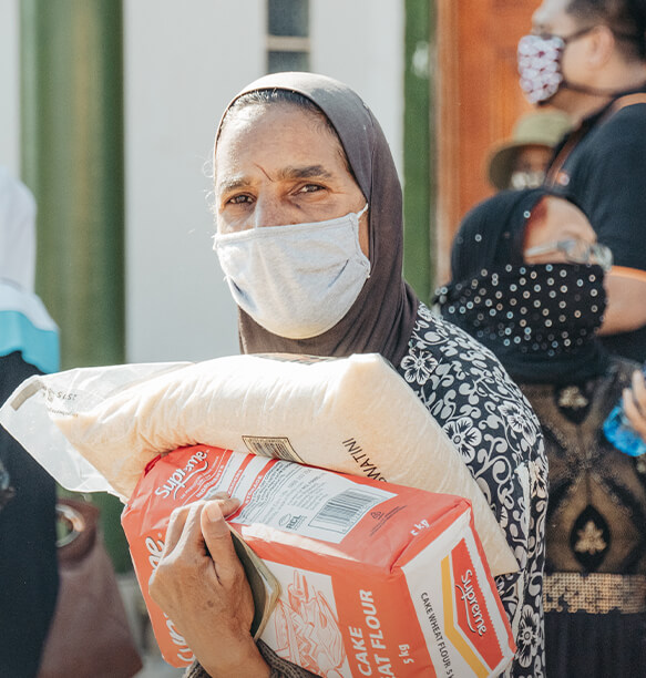 A woman wearing a face mask holding bags of flour and rice during a relief distribution event.