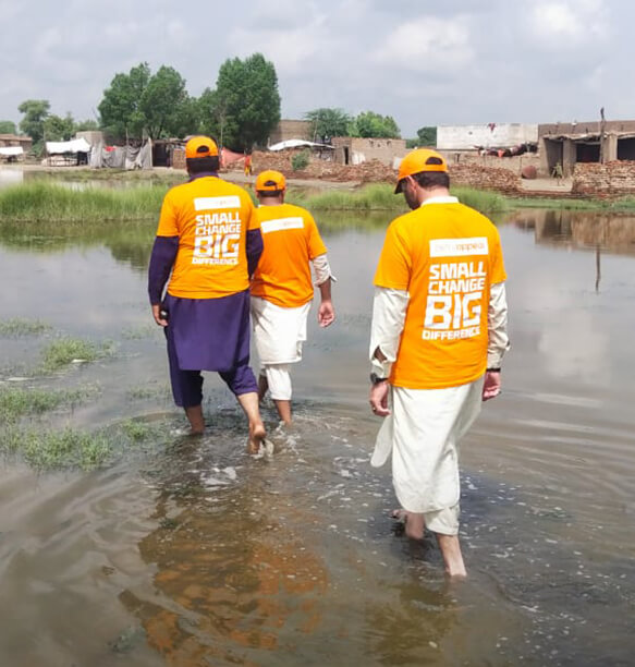 Volunteers walking through floodwaters, wearing matching 'Small Change Big Difference' T-shirts.