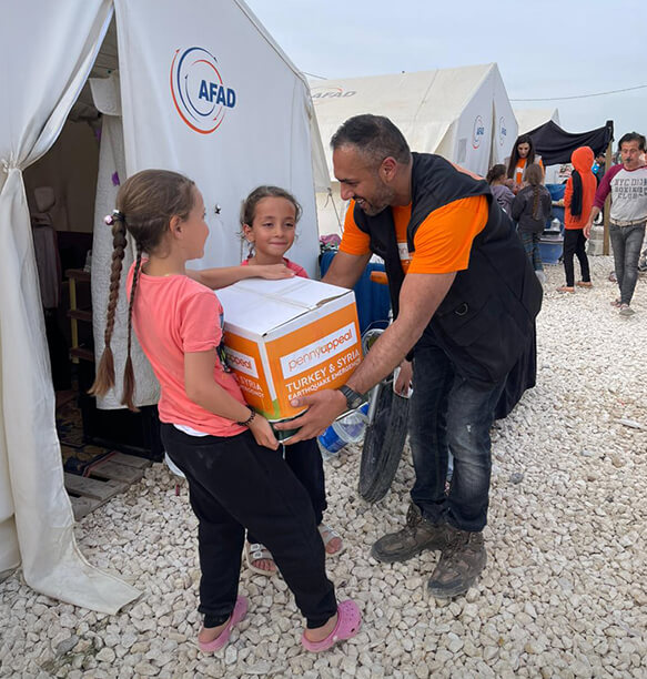 A volunteer handing a care package to two girls in a refugee camp.