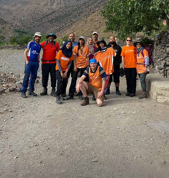 A group of volunteers posing together in a mountainous area, all wearing matching orange T-shirts.